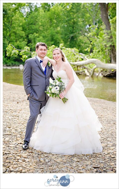 Bride and groom smiling at the camera and posing near Rocky River at Mill Stream Park in Valley City, Ohio after their wedding 