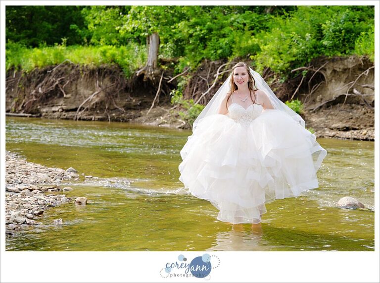 Bride standing in Rocky River in her wedding dress which is raised on a sunny June day after her wedding in Valley City Ohio