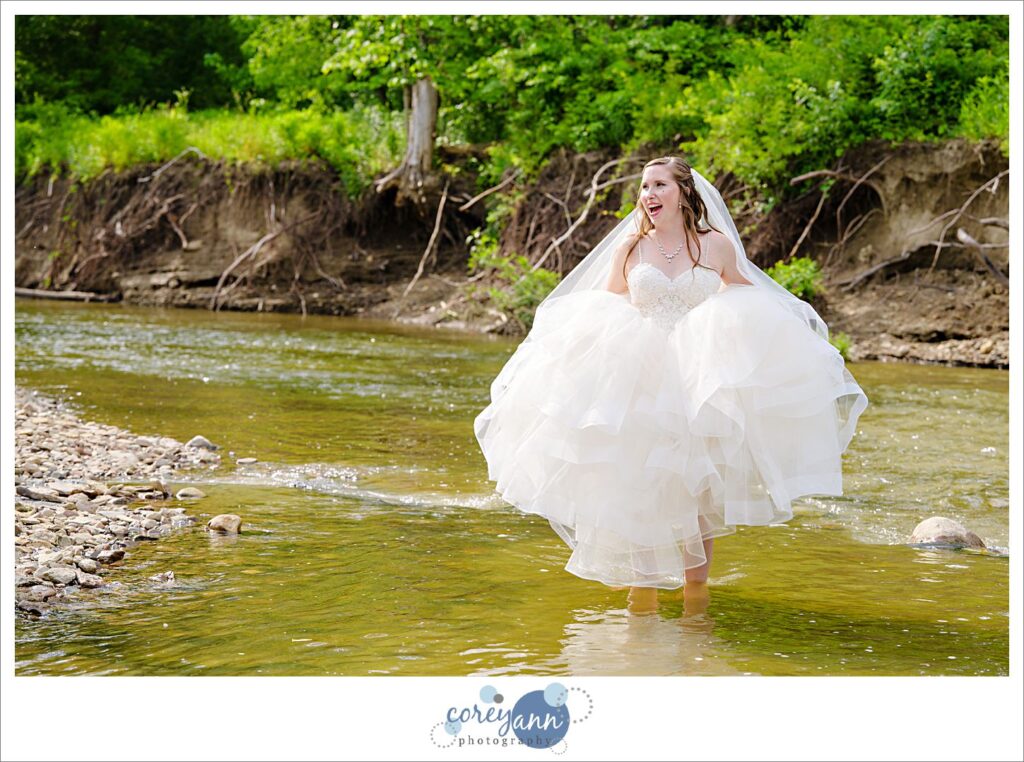Bride standing in Rocky River in her wedding dress which is raised on a sunny June day after her wedding in Valley City Ohio