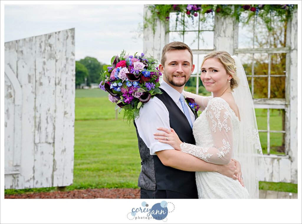 Bride and groom posing at the altar outside after their wedding at Nickajack Farms in Ohio bride is wearing a long sleeved white lace wedding gown and posing with her arms around her groom who is wearing a vest and rolled up sleeves