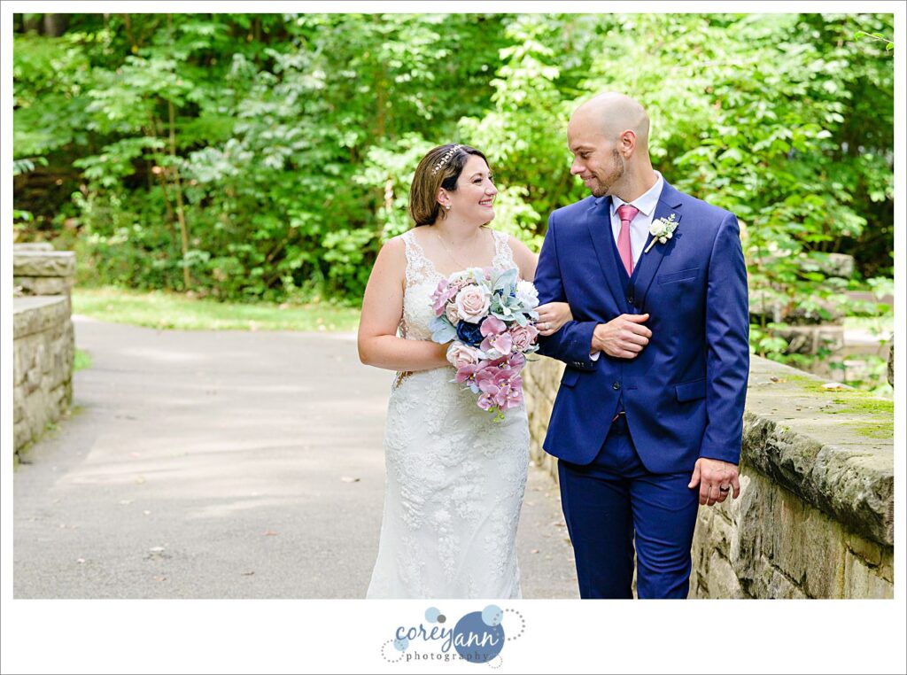 Wedding photos of a bride in a beaded lace gown and a groom in a blue suit with a pink tie at David Fortier River Park in Olmsted Falls in August 