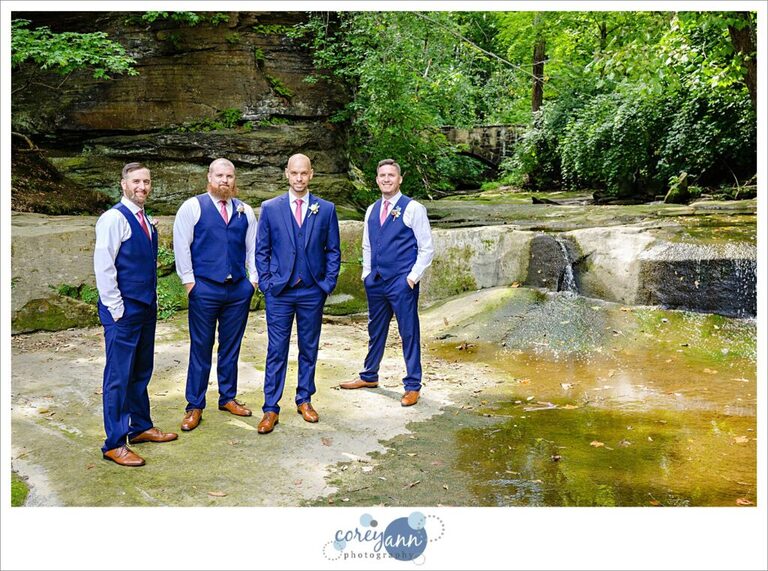 Groom and groomsman standing near a waterfall wearing blue suits in Olmsted Falls after a wedding