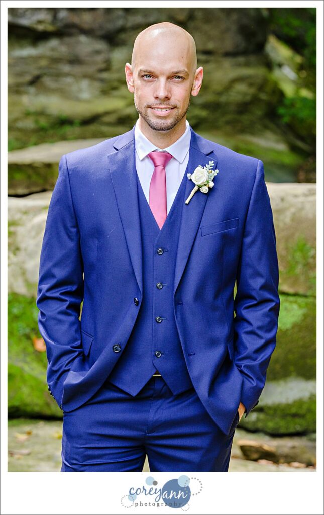Groom posing after a wedding at David Fortier River Park in Olmsted Falls wearing a blue suit with a vest and pink tie in August