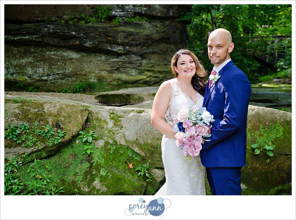 Wedding photos of a bride in a beaded lace gown and a groom in a blue suit with a pink tie at David Fortier River Park in Olmsted Falls in August 