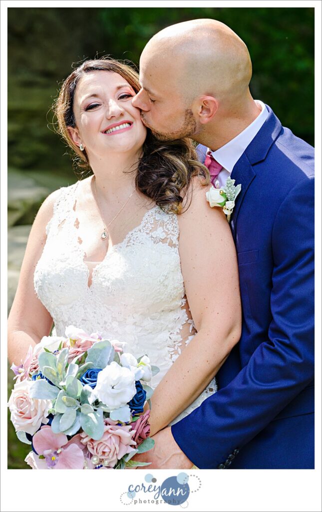 Wedding photos of a bride in a beaded lace gown and a groom in a blue suit with a pink tie at David Fortier River Park in Olmsted Falls in August 