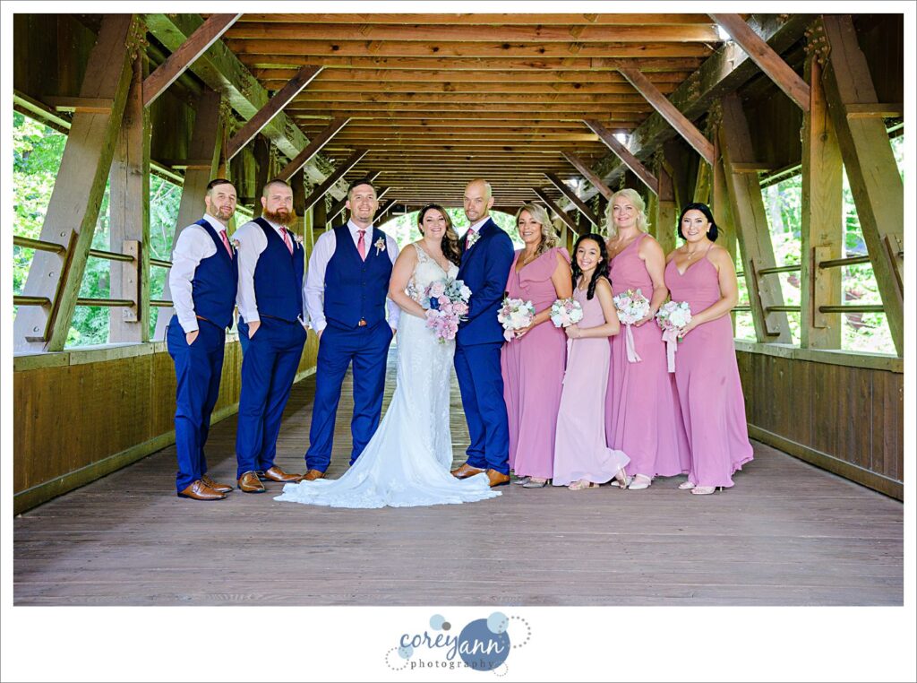 Blue and pink bridal party posing on a covered bridge in Olmsted Falls after wedding