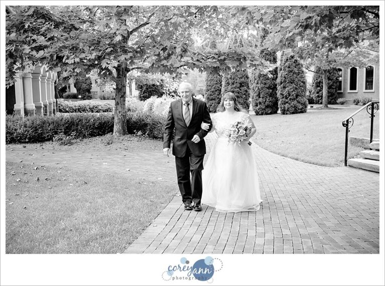 Black and white photo of bride and her father walking down the aisle