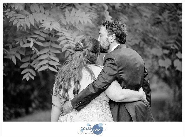 Groom kisses bride on forehead while walking the grounds at Gervasi Vineyard in Ohio after their wedding