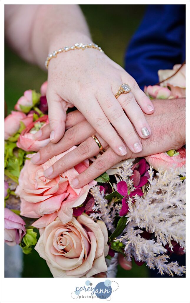Bride and groom place hands over each other on top of bouquet 