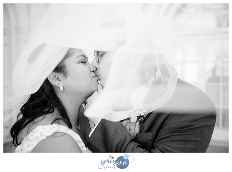 Bride and groom posing underneath the bride's veil in Ohio after wedding ceremony at Manakiki Golf Course