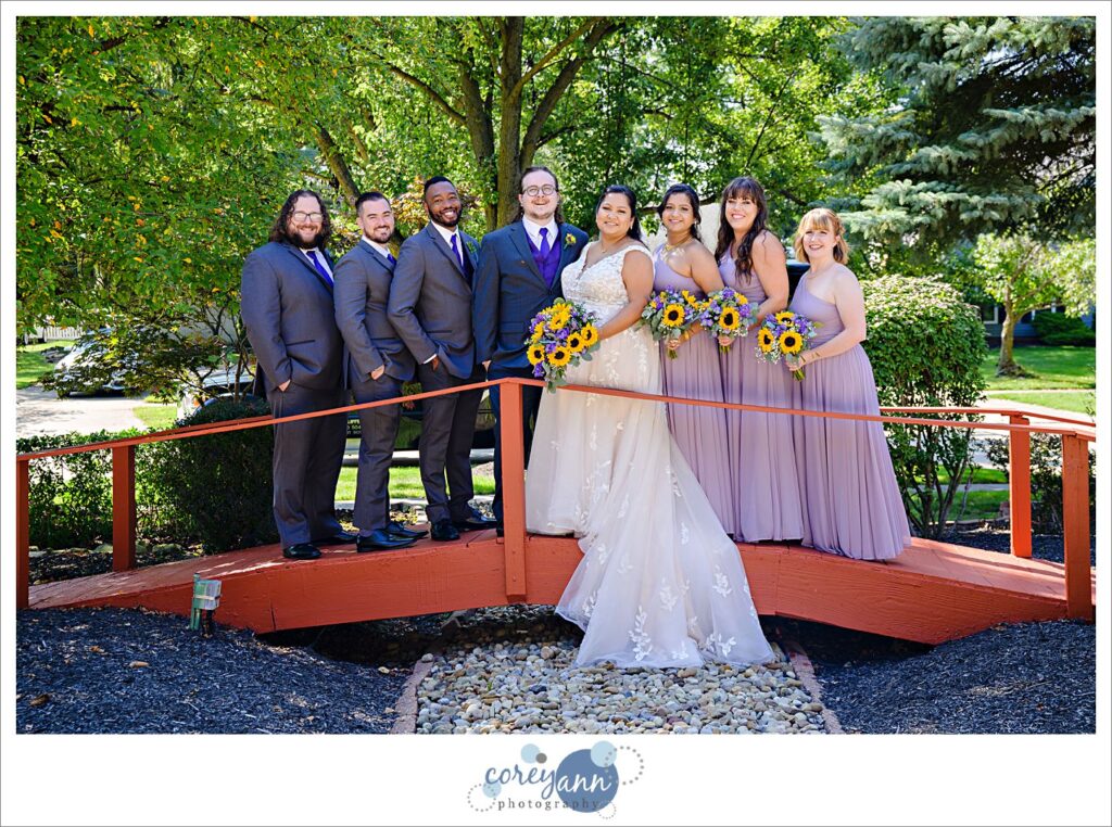 Bridal Party posing on a small red bridge at the bride's parents house after wedding 