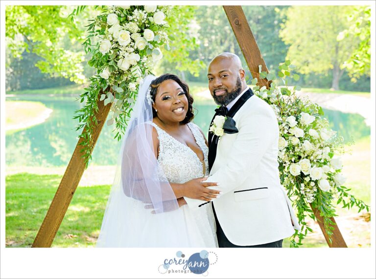Bride and Groom smiling in front of a wedding arch shaped like a triangle at Sun Valley wedding venue in Chagrin Falls Ohio