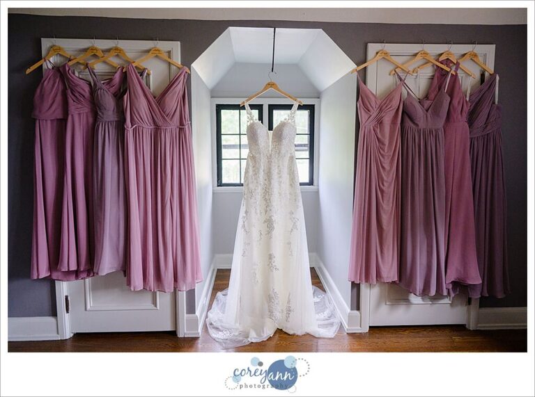 Bride's Mori Lee wedding dress hanging up alongside bridesmaids Azazie pink and lavender gowns