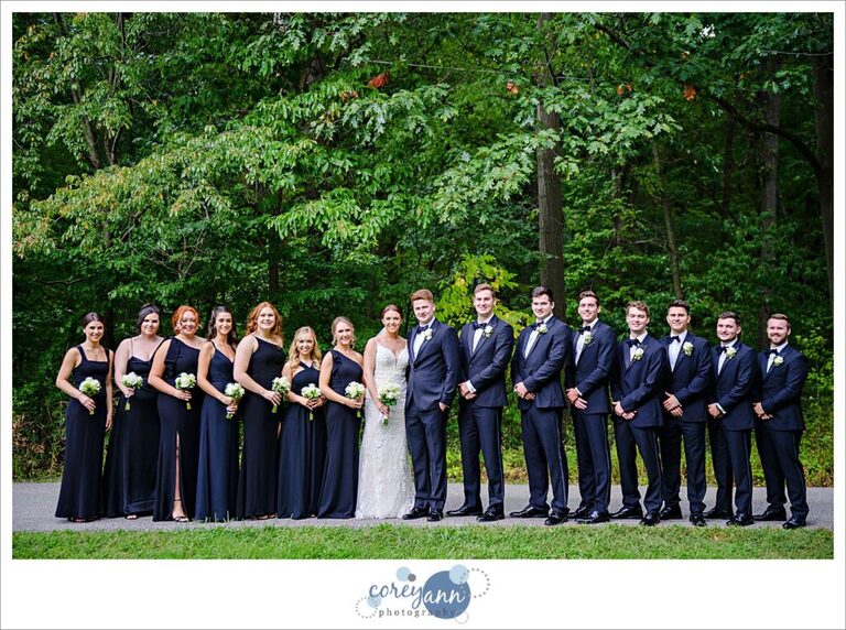 Large bridal party wearing black and white and bride and groom pose for a portrait at Huntington Reservation in Ohio