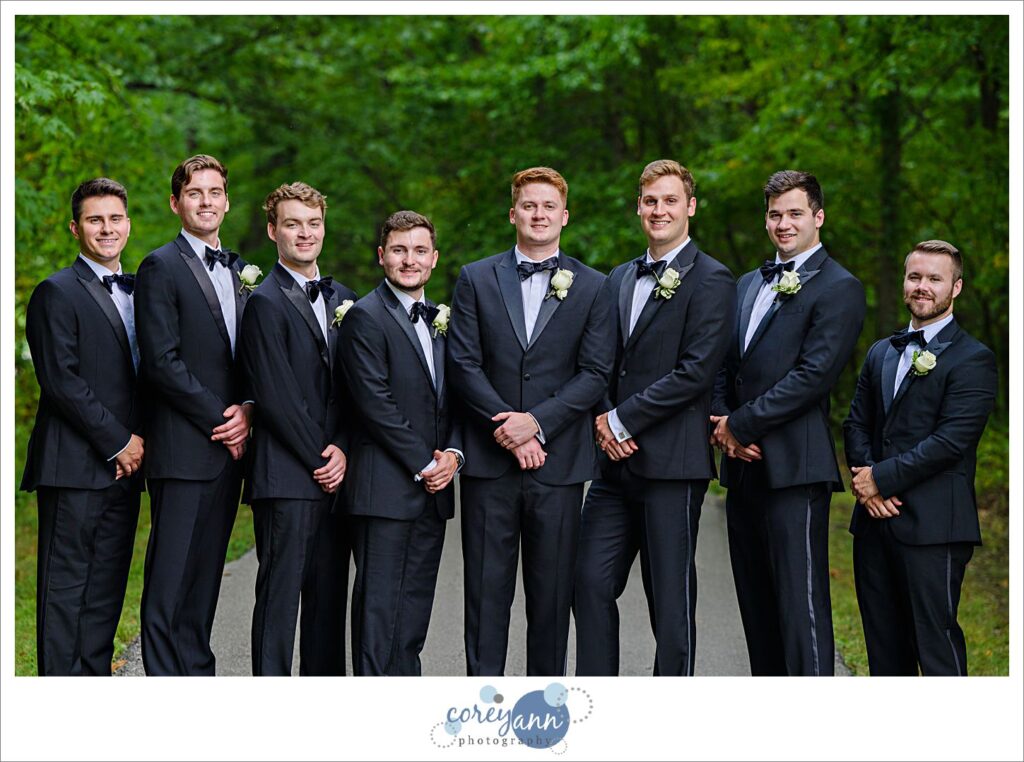 Groom and Groomsman wearing black tuxes pose for photos at Huntington Reservation in Ohio
