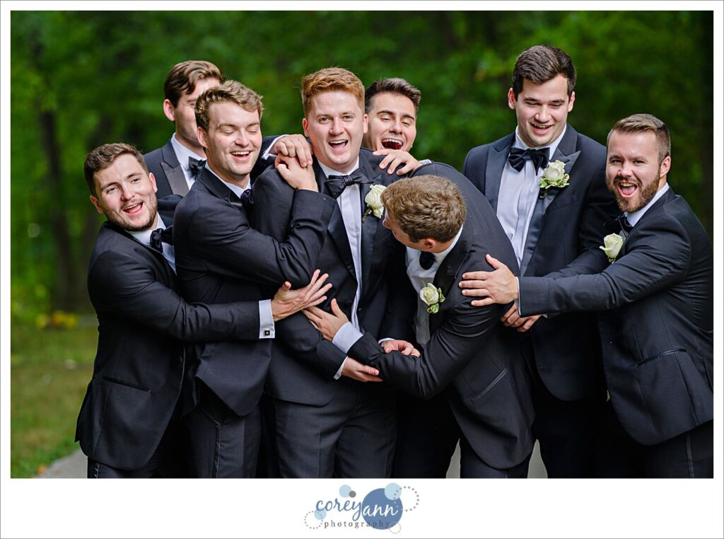 Groom and Groomsman wearing black tuxes pose for photos at Huntington Reservation in Ohio