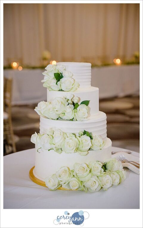 Simple but elegant white wedding cake decorated with white roses by Top Tier Cakes displayed at wedding reception at Emerald Event Center in Avon Ohio