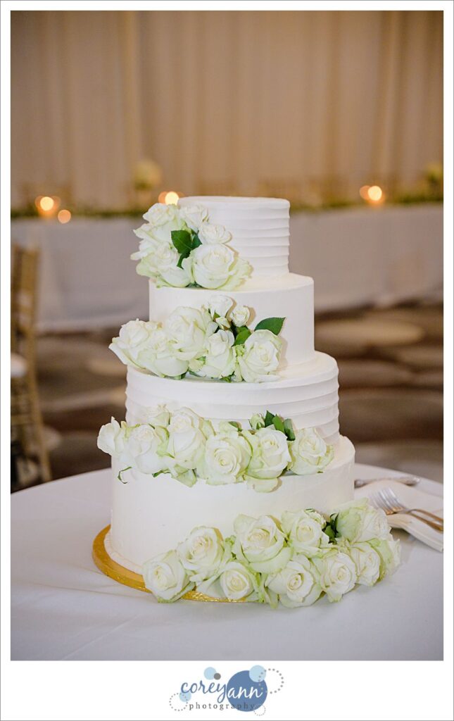 Simple but elegant white wedding cake decorated with white roses by Top Tier Cakes displayed at wedding reception at Emerald Event Center in Avon Ohio