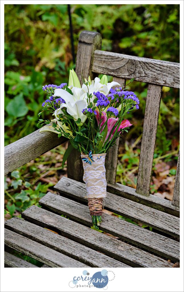 Photo of a bridal wedding bouquet on a bench that is pink and purple and white with lilies. 