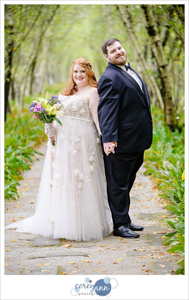 Wedding portrait with a bride and groom standing back to back posing by trees in Akron Ohio on a September day. 