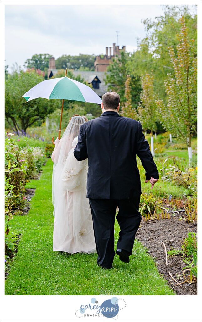 Groom holding an umbrella over his bride while walking through the rose garden near Stan Hywet Hall and Gardens in Akron Ohio