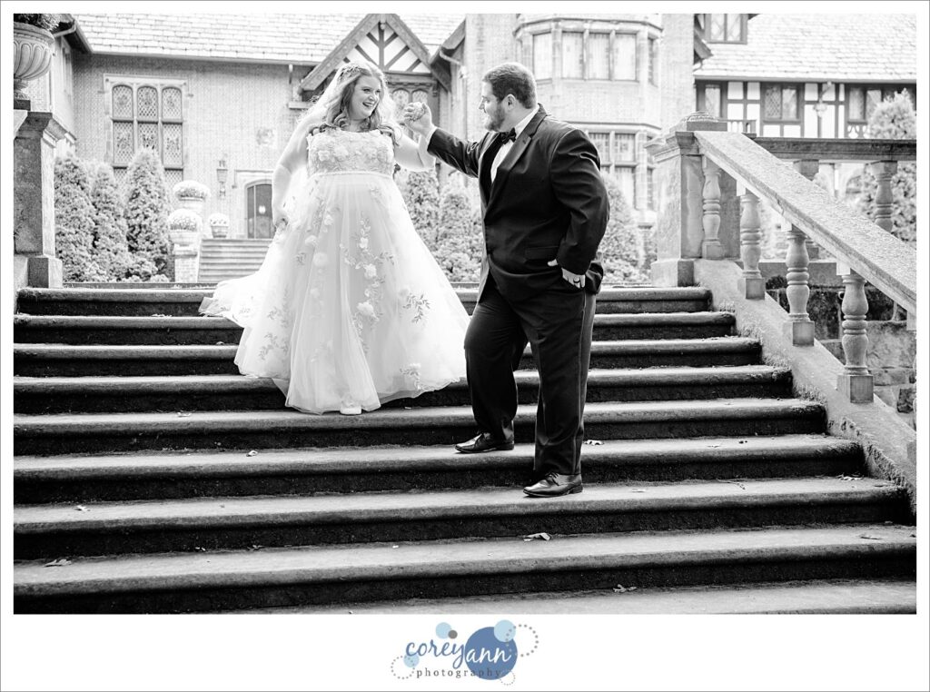 Groom helping a bride down the stairs behind Stan Hywet Hall and Gardens in black and white. 
