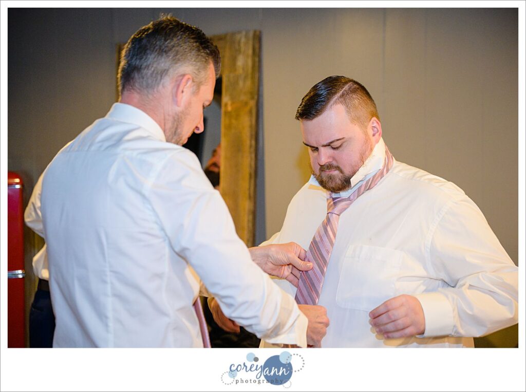 Groom's brother in law helping him with his pink tie before the wedding ceremony in Akron Ohio