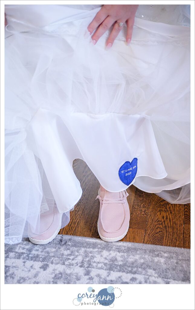Bride showing her blue heart with I Love You, Dad sewn in his handwriting for her something blue and wearing pink Hey Dudes