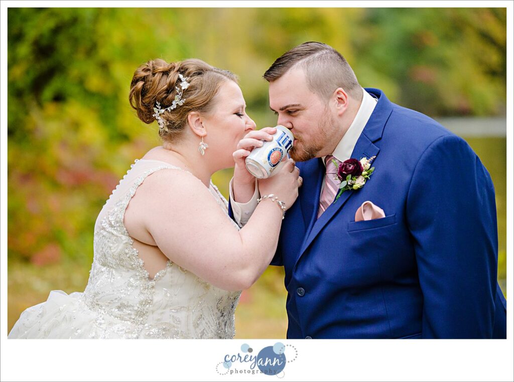 Bride and groom jokingly drinking beer with their arms intertwined