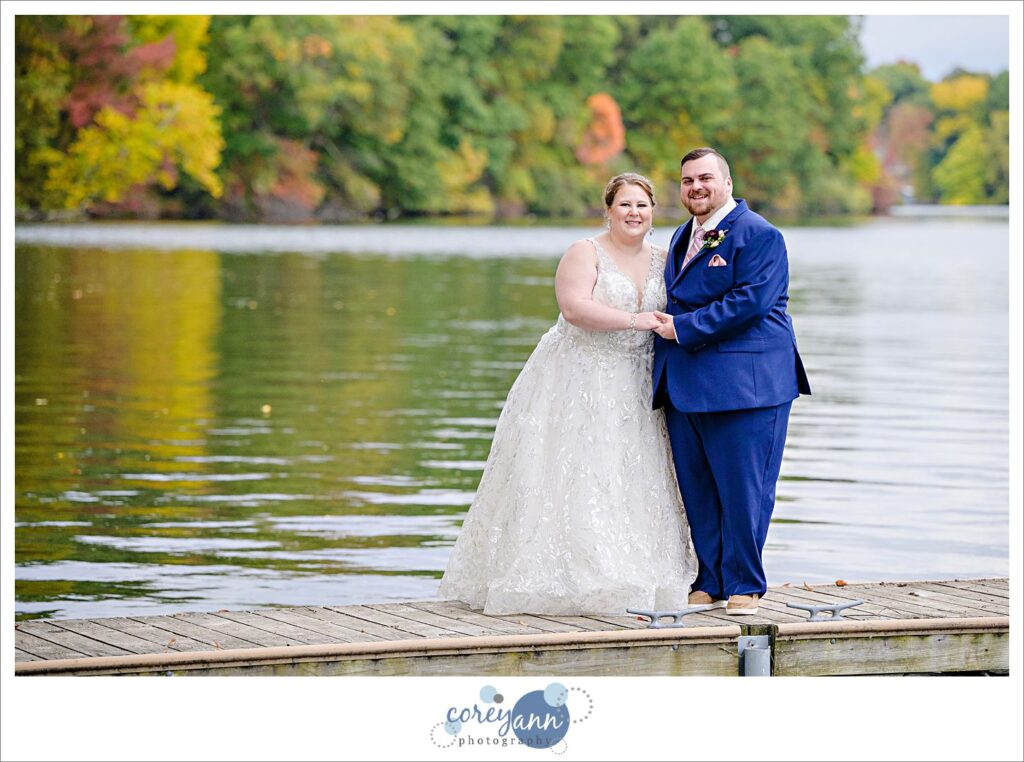 Bride and groom posing on a dock on Turkeyfoot Lake with fall foilage behind them in Akron Ohio