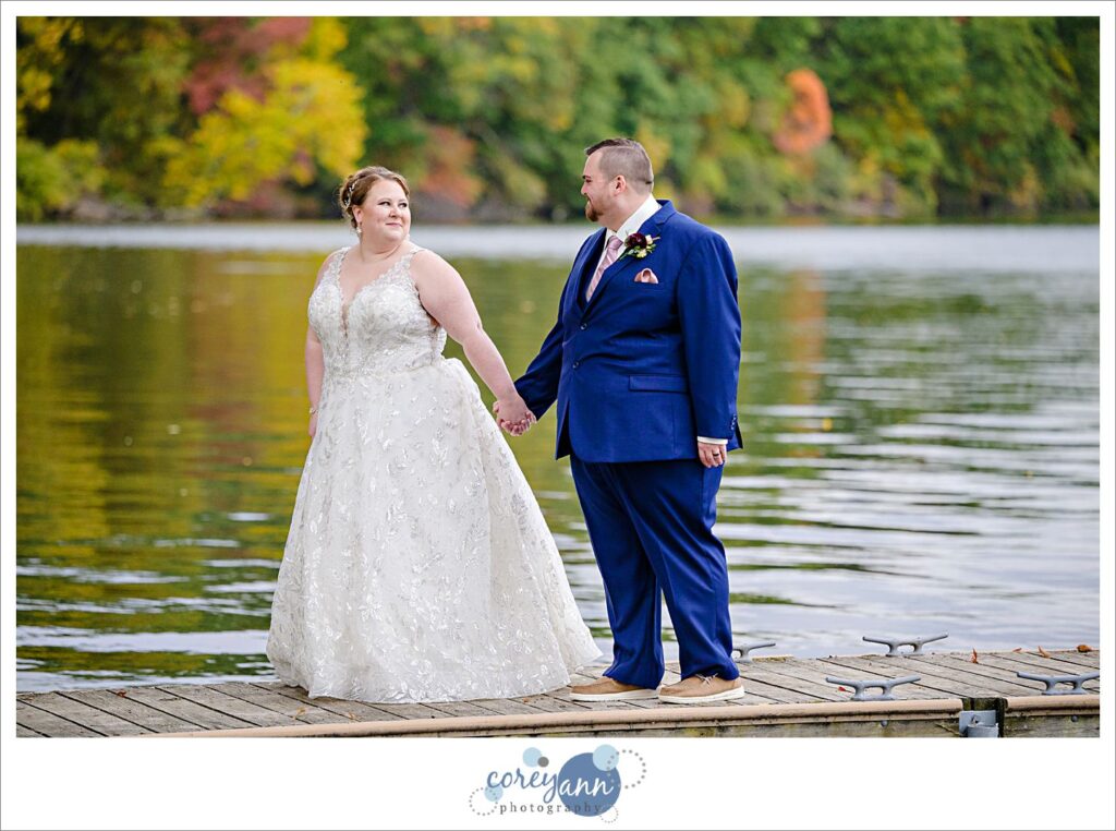 Bride and groom posing on a dock on Turkeyfoot Lake with fall foilage behind them in Akron Ohio