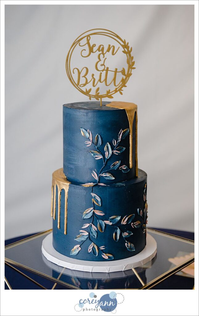 Modern navy and gold two tier wedding cake with floral leaf pattern and a gold name topper