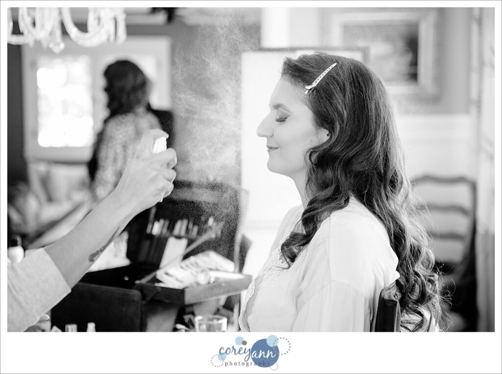 black and white photo of a bride sitting in a chair getting her makeup done before her wedding