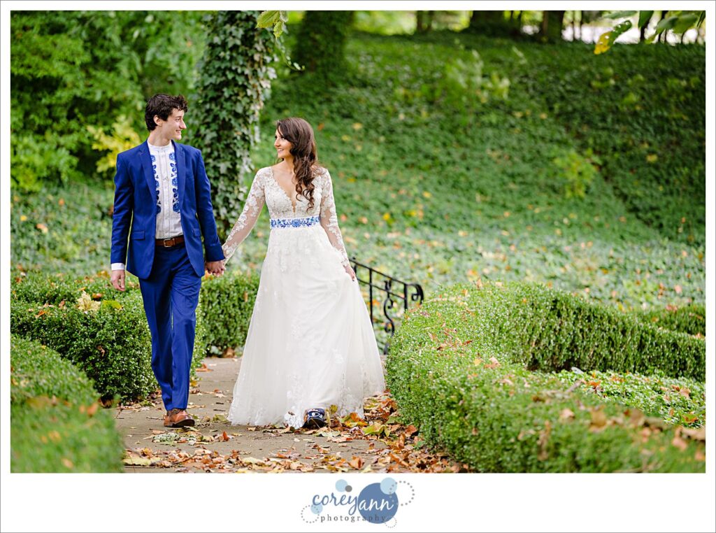 Bride and groom holding hands and walking on a leaf strewn path in October before their Cleveland wedding.