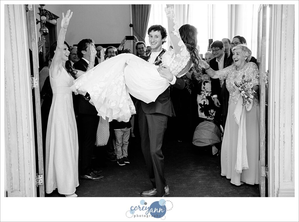 Groom carrying bride over threshold at October wedding reception at Bohemian National Hall in Cleveland Ohio