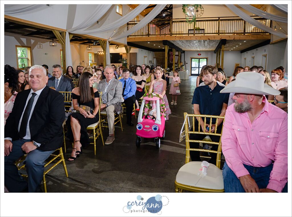 Flower girl in decorated cozy coupe being pushed down the aisle